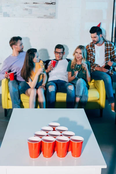 Plastic cups on table and young friends drinking alcohol beverages behind — Stock Photo