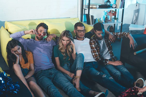 Borrachos jóvenes hombres y mujeres amigos sentados en el suelo después de la fiesta en casa - foto de stock