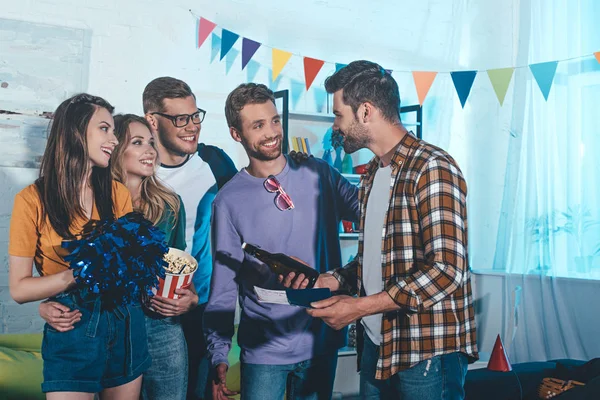 Happy young people looking at friend with passport and ticket at home party — Stock Photo