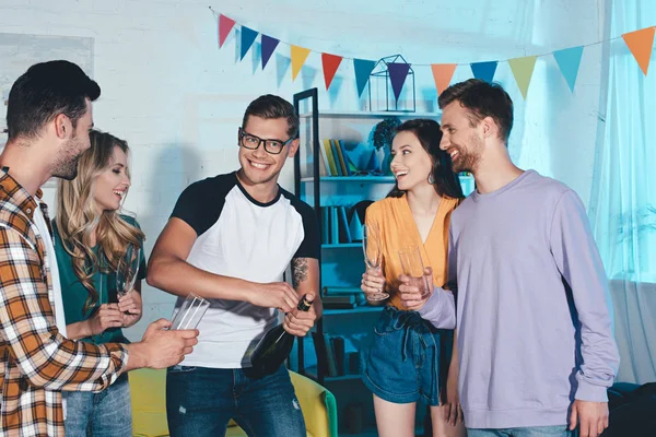 Happy young friends opening bottle of wine at home party — Stock Photo