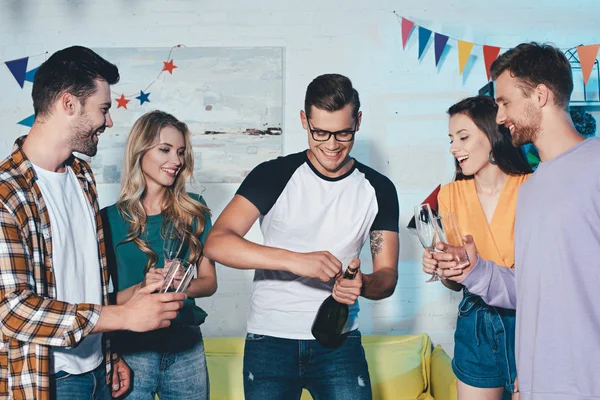 Felizes jovens amigos masculinos e femininos abrindo garrafa de vinho em casa festa — Fotografia de Stock