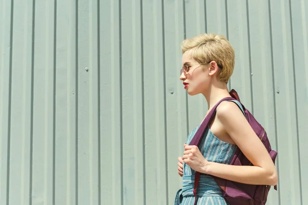 Fille aux cheveux courts posant avec sac à dos au mur — Photo de stock