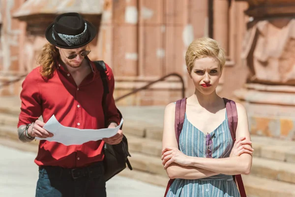 Tourist looking at map while confused girlfriend with crossed arms standing near — Stock Photo