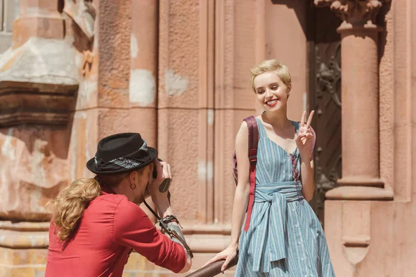 Man taking photo of happy girlfriend showing victory sign — Stock Photo