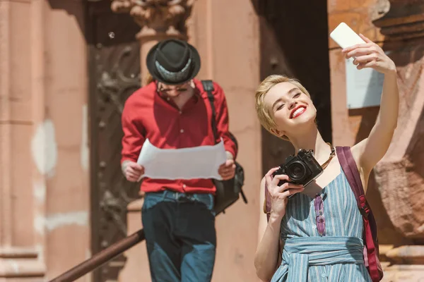 Fille avec caméra prendre selfie sur smartphone tandis que l'homme regardant la carte — Photo de stock