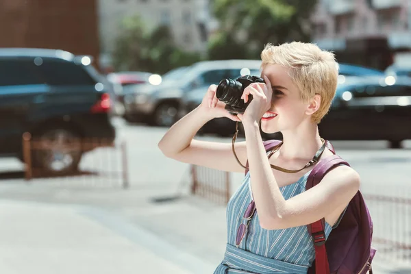 Viajero con mochila tomando fotos en cámara en la ciudad - foto de stock