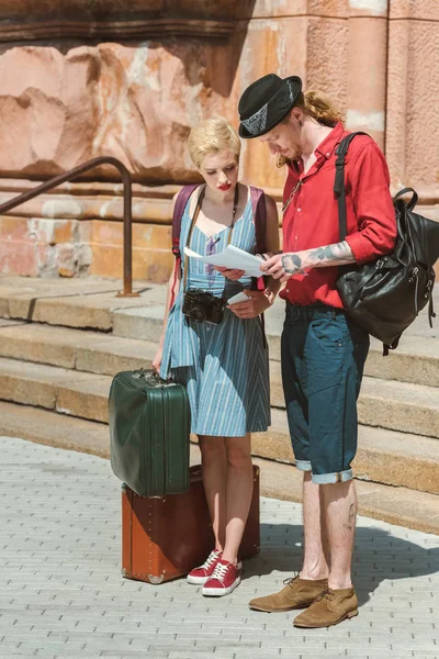 Couple of travelers with backpacks and retro suitcases looking at map — Stock Photo
