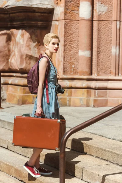 Красивая девушка с рюкзаком, фотоаппаратом и винтажными чемоданами — стоковое фото