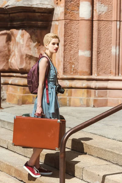 Beautiful girl with backpack, camera and vintage suitcases — Stock Photo