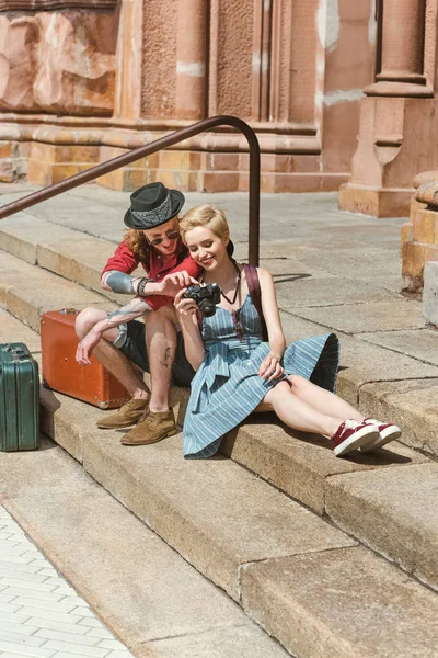 Couple of travelers with vintage suitcases sitting on stairs and looking at camera — Stock Photo