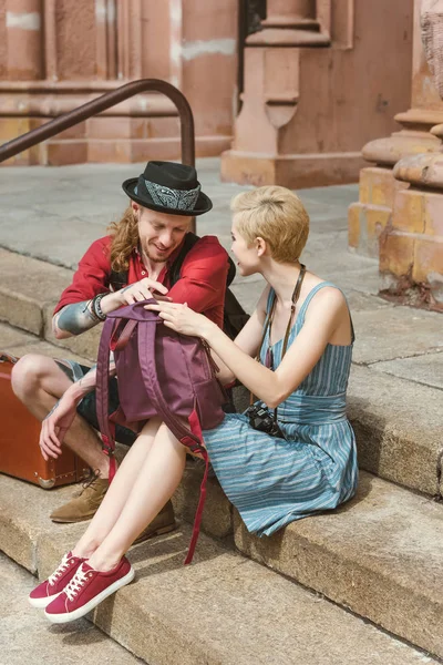 Beautiful tourists with backpacks sitting on stairs in city — Stock Photo