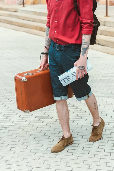 Обрізаний вид чоловіка з туристичною газетою та старовинною валізою — стокове фото
