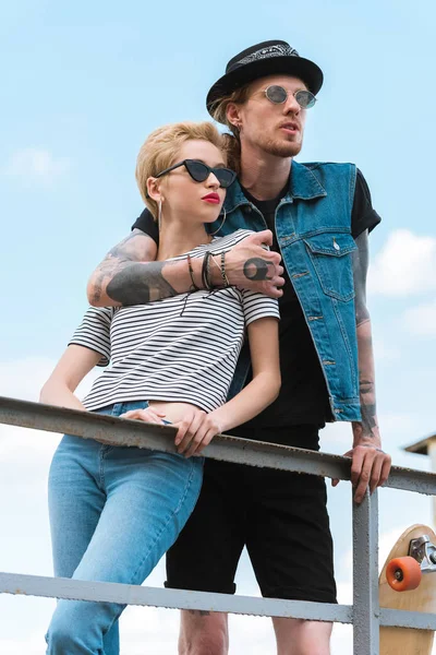 Boyfriend with tattoos hugging stylish girlfriend and they leaning on railing — Stock Photo
