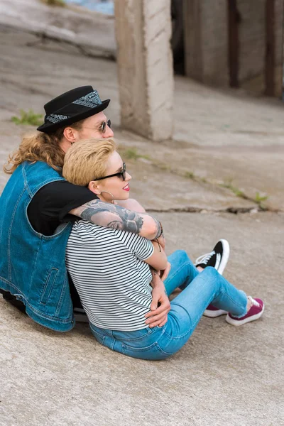 Vue latérale du petit ami avec des tatouages étreignant petite amie élégante et ils regardent loin — Photo de stock