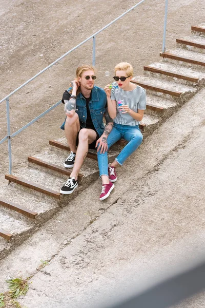 Vista de ángulo alto de novia y novio sentado en las escaleras y divertirse con burbujas de jabón - foto de stock