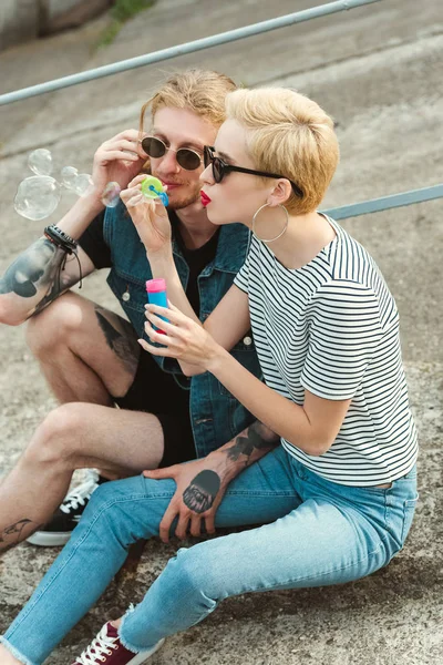 Парень с татуировками и стильная девушка веселятся с мыльными пузырями — стоковое фото