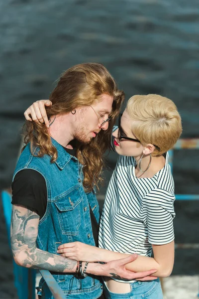 Vue grand angle de petit ami avec des tatouages et copine élégante va embrasser sur le pont — Photo de stock