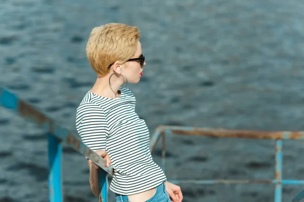 Stilvolles Mädchen mit Sonnenbrille lehnt an Geländer am Fluss und schaut weg — Stockfoto