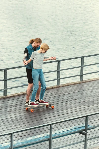 High angle view of boyfriend with tattoos teaching skating stylish girlfriend — Stock Photo