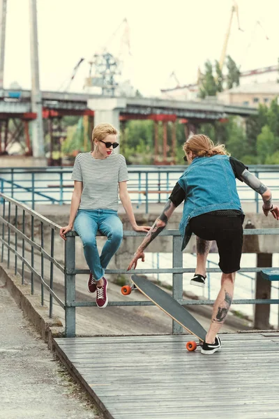 Tätowierter Freund beim Schlittschuhlaufen vor stilvoller Freundin — Stockfoto