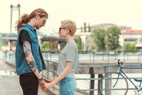 Boyfriend with tattoos and stylish girlfriend holding hands and touching with foreheads — Stock Photo