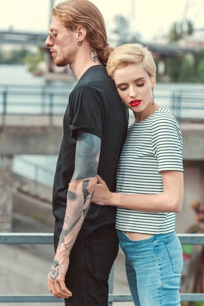 Novia elegante abrazando novio tatuado de vuelta en el puente — Stock Photo
