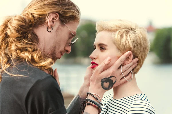Affectionate tattooed boyfriend and stylish girlfriend looking at each other on bridge — Stock Photo