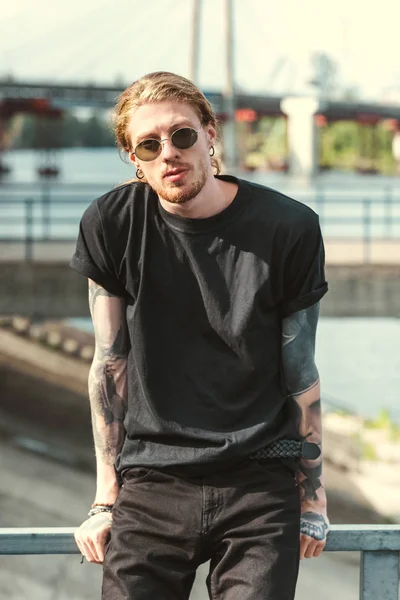 Красивий стильний татуйований чоловік дивиться на камеру в сонцезахисних окулярах — стокове фото