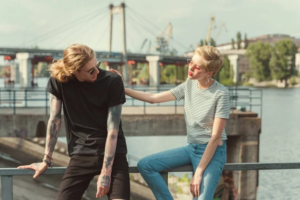 Stylish girlfriend palming boyfriend with tattoos on bridge — Stock Photo