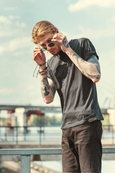 Bel homme tatoué élégant portant des lunettes de soleil sur le pont — Photo de stock