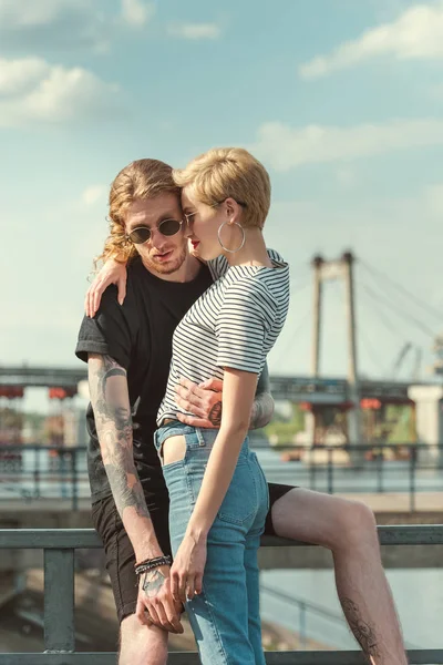 Novio con tatuajes y elegante novia abrazándose en el puente - foto de stock
