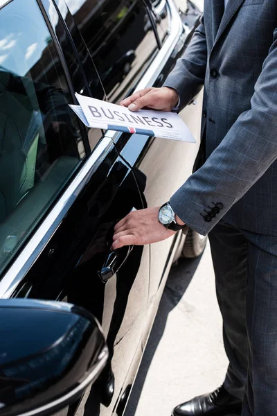 Cropped shot of businessman with newspaper opening car door on street — Stock Photo