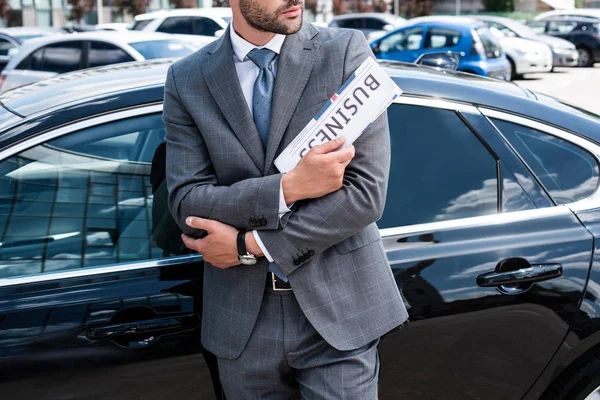 Vista parcial del hombre de negocios con periódico de pie en el coche en la calle - foto de stock