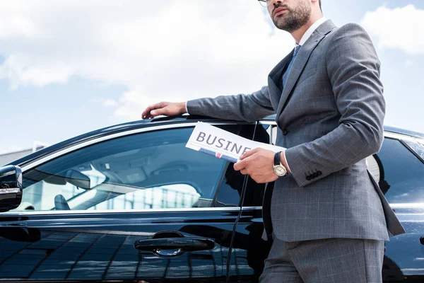 Teilansicht eines Geschäftsmannes mit Zeitung, der am Auto auf der Straße steht — Stockfoto