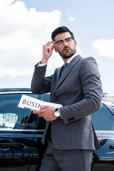 Vista lateral del hombre de negocios con periódico de pie en el coche en la calle - foto de stock