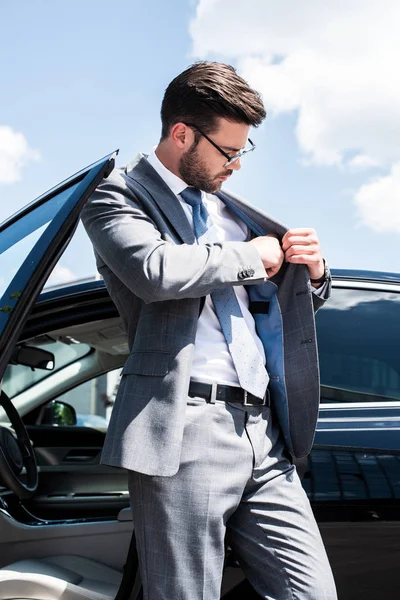 Geschäftsmann zieht etwas aus Tasche, während er neben Auto auf der Straße steht — Stockfoto