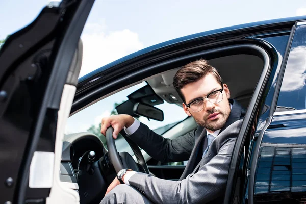 Pensive businessman in eyeglasses looking away while sitting in car — Stock Photo