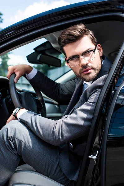 Pensive businessman in eyeglasses looking away while sitting in car — Stock Photo