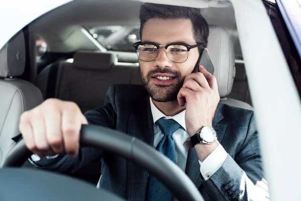 Retrato de un hombre de negocios sonriente hablando en el teléfono inteligente mientras conduce el coche - foto de stock