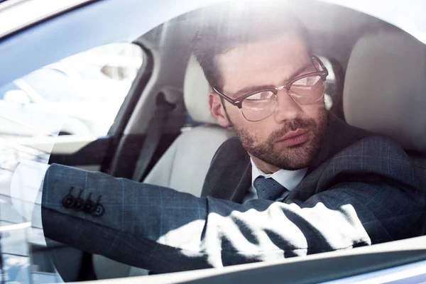 Vista lateral del hombre de negocios en anteojos mirando hacia otro lado mientras conduce el coche - foto de stock