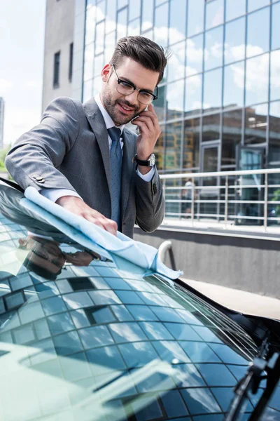 Усміхнений бізнесмен говорить на смартфоні, прибираючи переднє скло ганчіркою — стокове фото