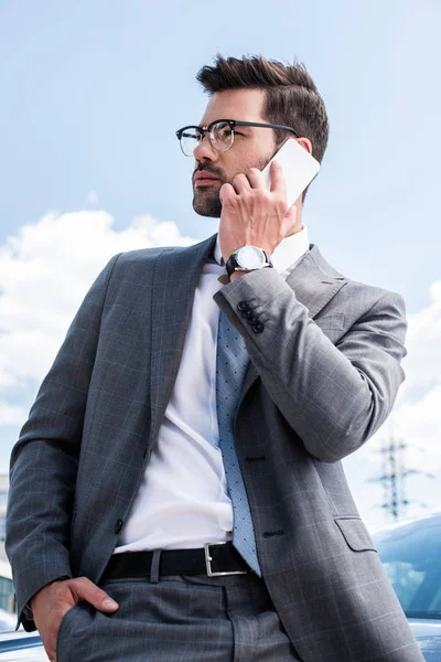 Businessman in eyeglasses talking on smartphone while standing near car on street — Stock Photo