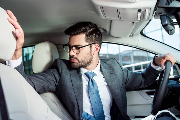 Uomo d'affari in occhiali guardando altrove durante la guida di auto — Foto stock