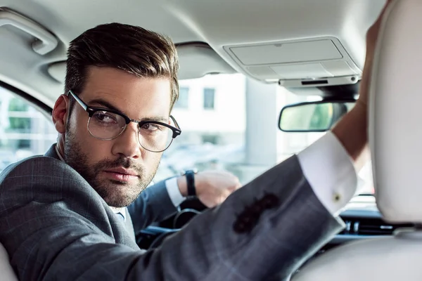 Бизнесмен в очках смотрит в сторону во время вождения автомобиля — стоковое фото