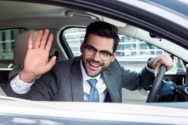Vue latérale de l'homme d'affaires joyeux saluant quelqu'un tout en conduisant une voiture — Photo de stock
