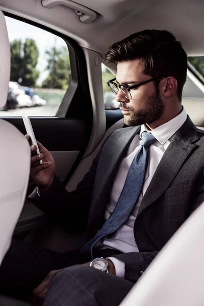 Seitenansicht eines selbstbewussten Geschäftsmannes mit Smartphone auf dem Rücksitz im Auto — Stockfoto