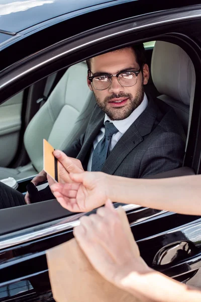 Partial view of businessman in car giving credit card to waiter with take away food — Stock Photo