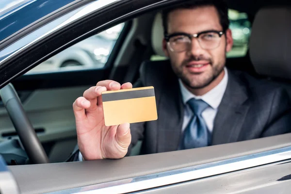 Enfoque selectivo de hombre de negocios mostrando la tarjeta de crédito en la mano mientras está sentado en el coche - foto de stock
