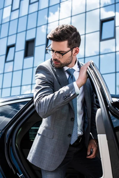 Молодий бізнесмен у костюмі та окулярах, що виходять з машини — стокове фото