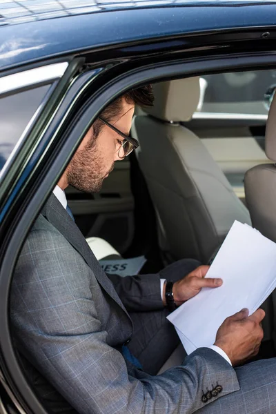 Side view of businessman with documents sitting on backseat of car — Stock Photo